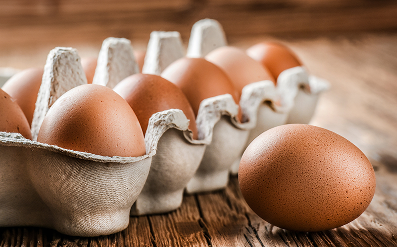 Ein offener Eierkarton mit braunen Eiern auf einem Holztisch, daneben ein einzelnes Ei.