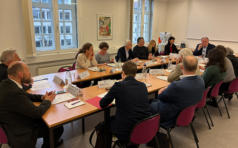 Besprechung mit mehreren Teilnehmenden an einem langen Konferenztisch in einem Sitzungsraum